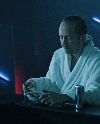 a man in a robe sits at a table with a can of red bull