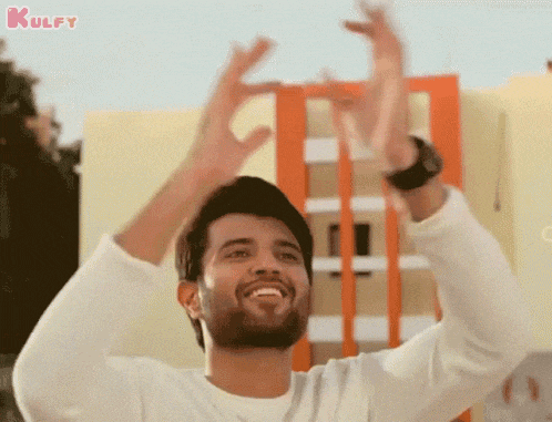 a man with his arms in the air is smiling and making a sign with his hands .