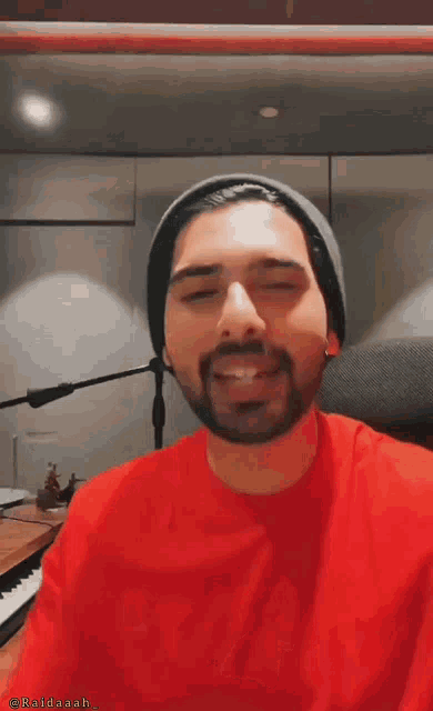 a man with a beard wearing a red shirt and a gray hat is making a funny face .