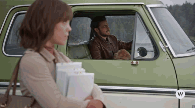 a man and a woman are sitting in a green car with a w logo on the side