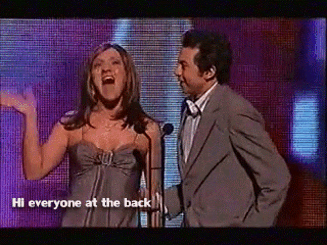 a man and a woman on a stage with hi everyone at the back