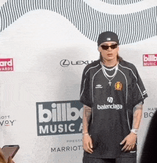 a man wearing a balenciaga shirt stands in front of a billboard music awards backdrop