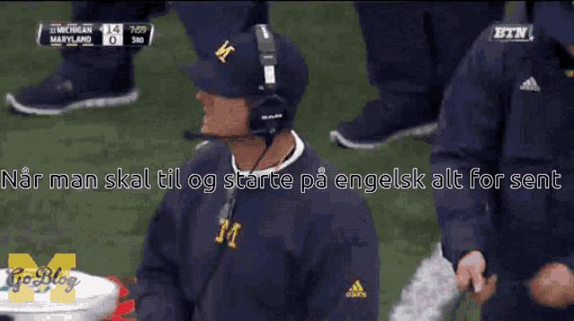 a man wearing a michigan hat and headphones stands on a field