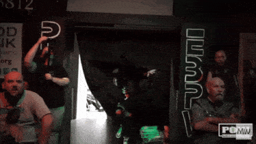 a group of people are watching a wrestler in a room with a sign that says pcmw