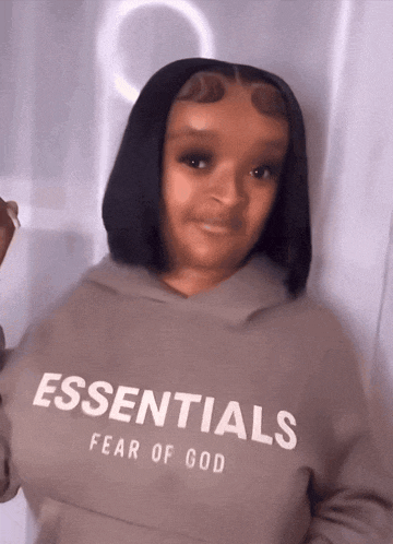 a woman wearing a hoodie that says essentials fear of god on it