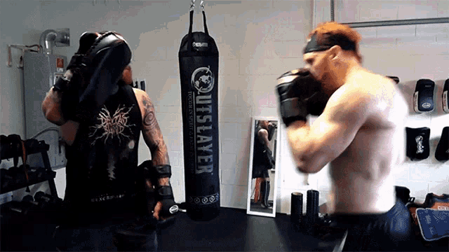 two men are boxing in front of a punching bag that says outslayer on it