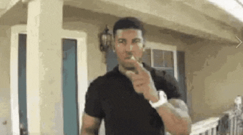 a man in a black shirt is standing in front of a house pointing at the camera .