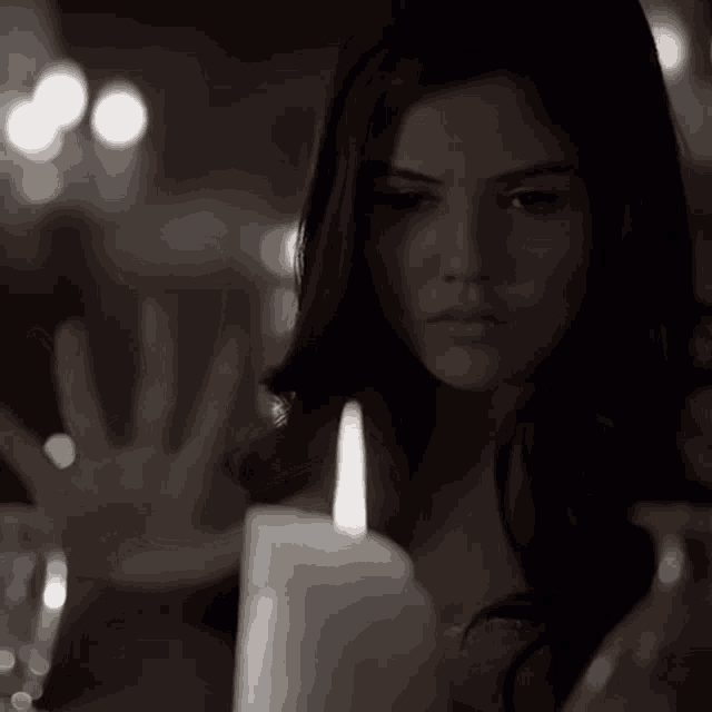 a woman holds her hand out towards a lit candle