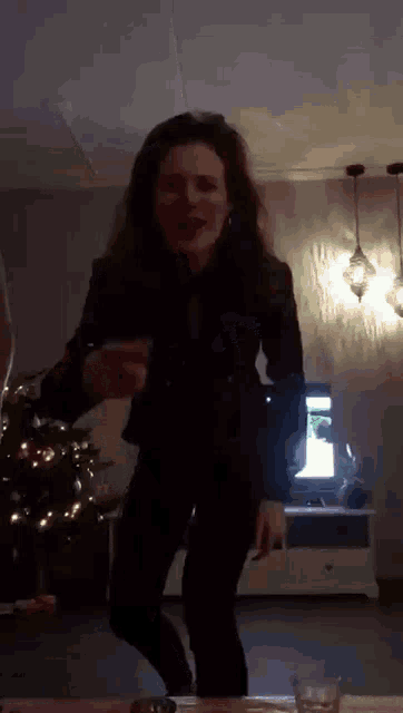 a woman is dancing in a living room with a christmas tree in the background .