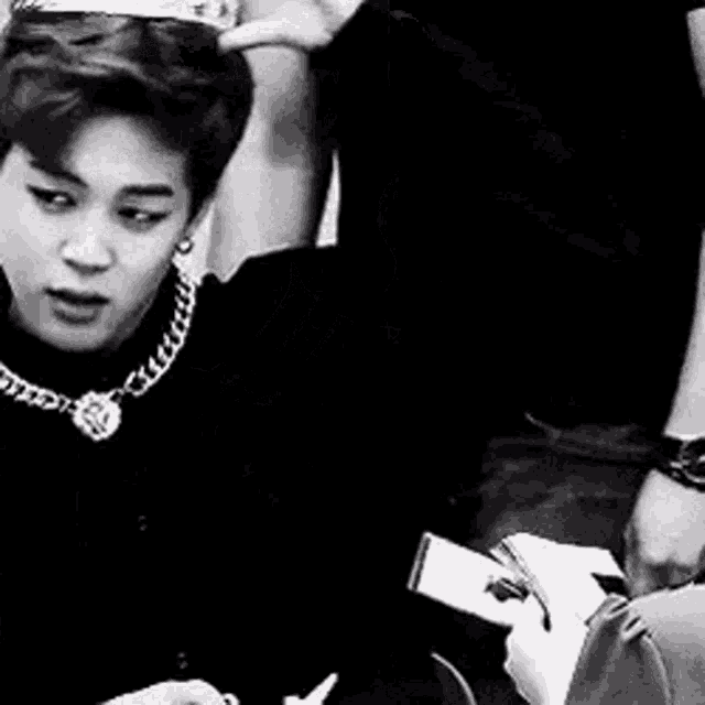 a black and white photo of a young man wearing a necklace holding a lollipop .