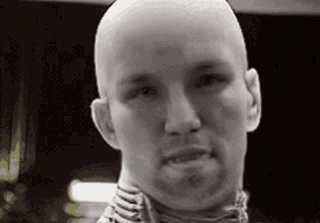 a bald man with a scarf around his neck is looking at the camera