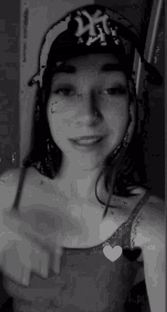 a black and white photo of a woman wearing a hat and a heart necklace .