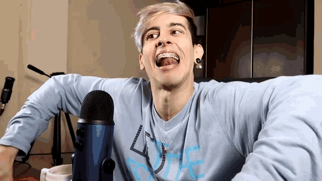 a man with braces on his teeth is sitting in front of a microphone with his mouth wide open
