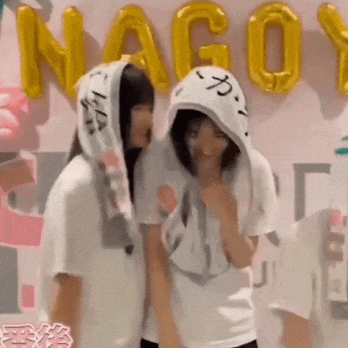 two girls are standing next to each other in front of a wall with the word nagoya on it .