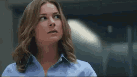 a woman in a blue shirt is looking up at something in a dark room .