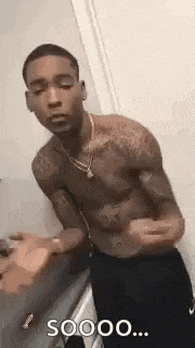 a shirtless man is standing in a bathroom with his arms outstretched and a necklace around his neck .