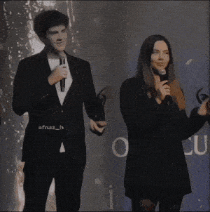 a man in a suit stands next to a woman holding a microphone with the hashtag efnaz_h on the bottom