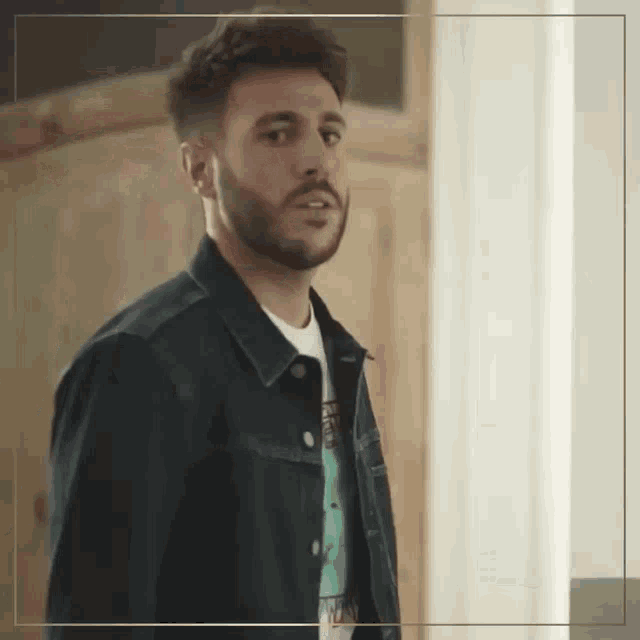 a man with a beard wearing a denim jacket and a t-shirt .
