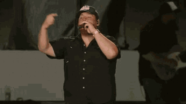 a man in a black shirt is singing into a microphone while wearing a hat that says eagles on it