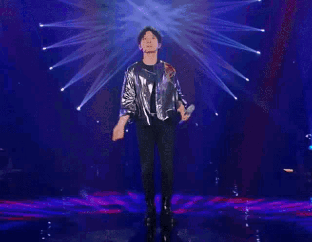 a man in a silver jacket is holding a microphone on a stage