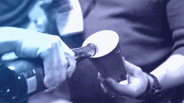 a person is opening a bottle of wine with a paper cup in their hand