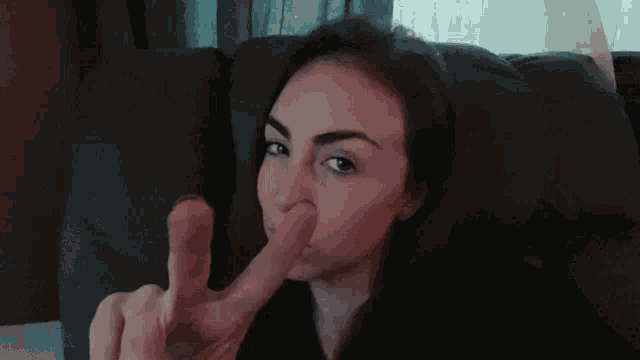a woman sitting on a couch holding her nose with her finger