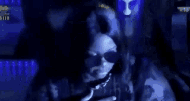 a woman wearing sunglasses is sitting in a dark room with a blue light behind her .