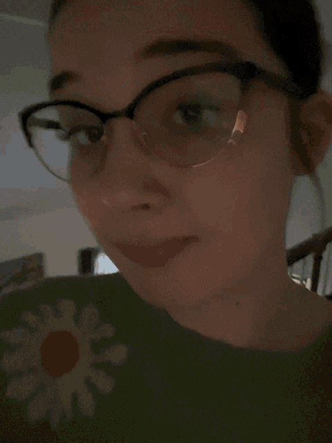 a woman wearing glasses and a green sweater has her tongue out