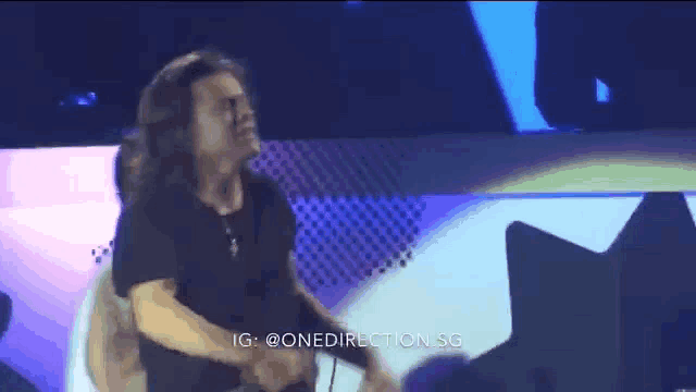 a man with long hair is dancing on a stage in front of a crowd .