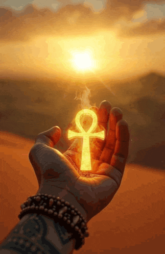 a hand is holding a glowing ankh symbol in front of the sun