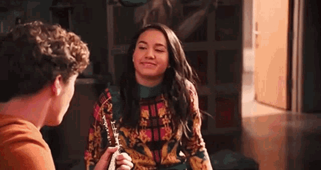 a man and a woman are sitting next to each other in a room and the woman is holding a guitar .