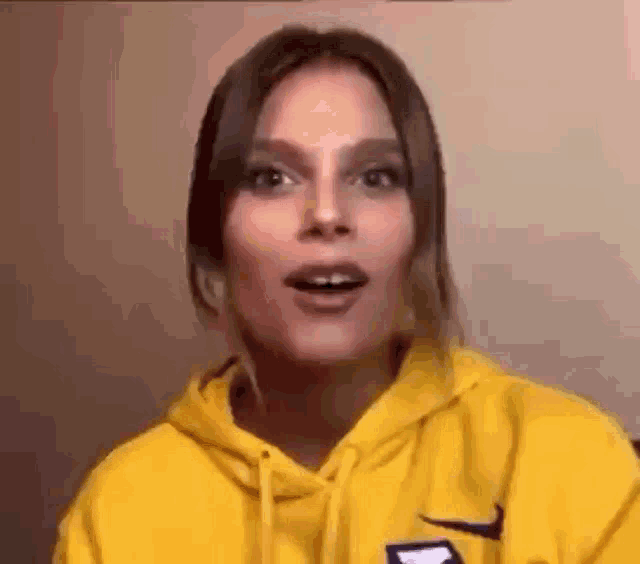 a woman wearing a yellow hoodie is making a funny face and looking at the camera .
