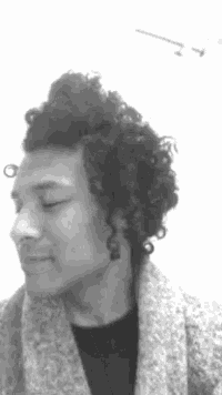 a black and white photo of a man with curly hair wearing a grey sweater