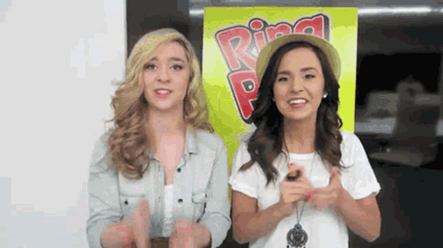 two young women are standing next to each other in front of a sign that says ring .