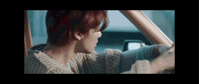 a man with red hair is driving a car with his hand out the window .