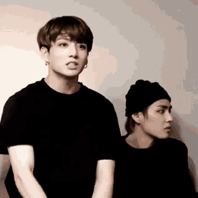 two young men are standing next to each other wearing black shirts and beanies .