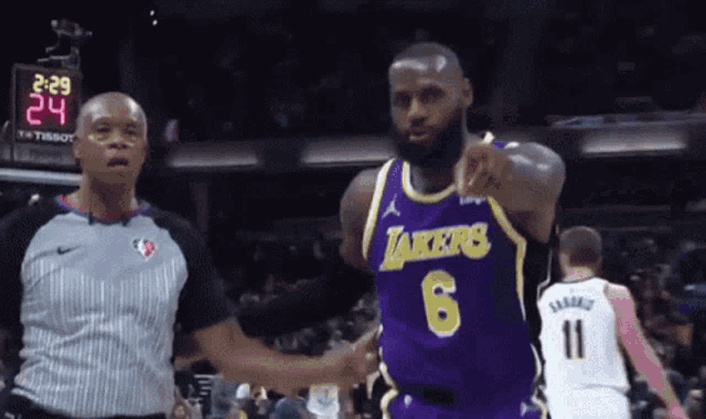 a basketball player wearing a lakers jersey is pointing at the referee