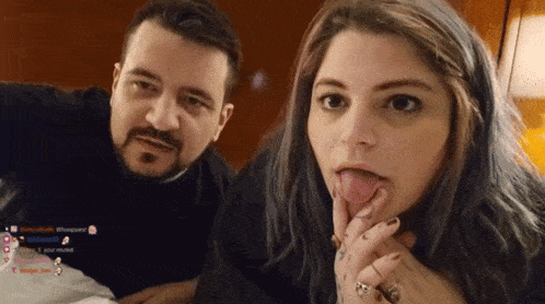 a man and a woman are sitting next to each other and the woman is sticking out her tongue