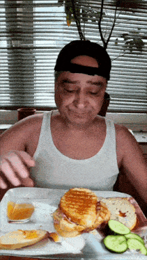 a man in a tank top is eating a sandwich with a knife and fork