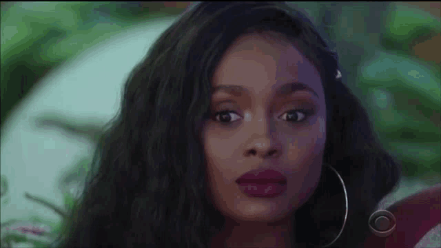 a close up of a woman 's face with a purple lip color and hoop earrings .