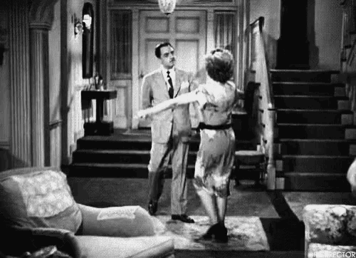 a black and white photo of a man and a woman dancing in a living room .