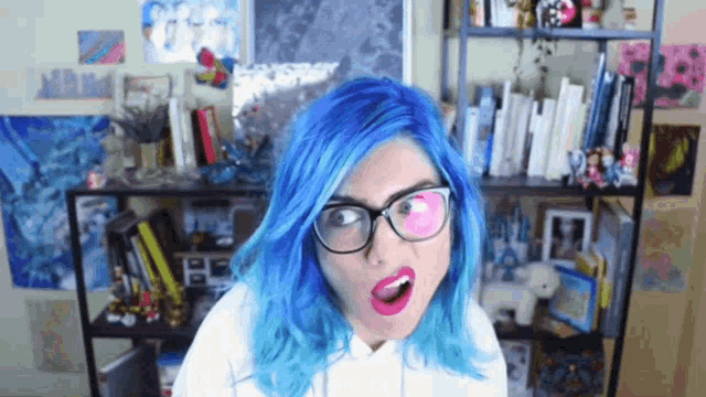 a woman with blue hair is wearing glasses and a white hoodie