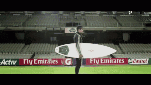 a man is holding a surfboard in front of a fly emirates sign