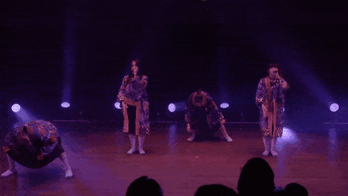 a group of people are performing on a stage with purple lights behind them