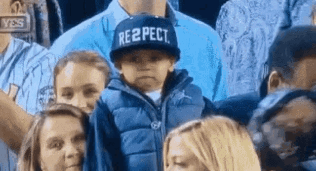 a young boy wearing a hat that says respect is standing in a crowd .