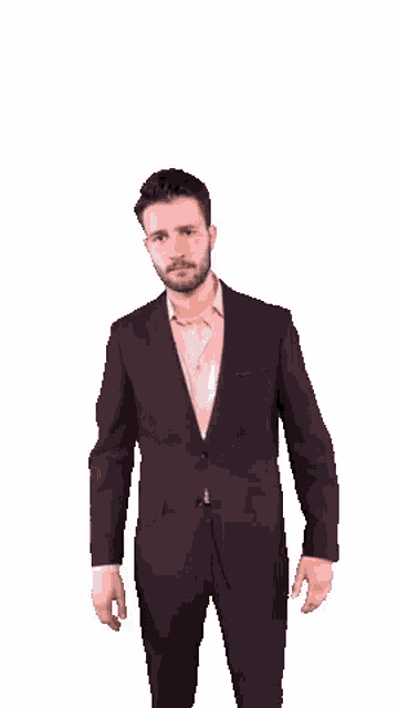 a man in a purple suit and a pink shirt is standing with his hands in his pockets .