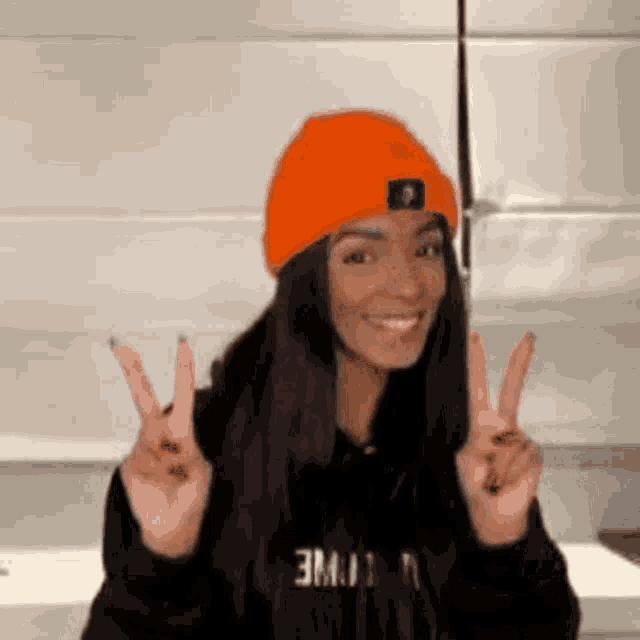 a woman wearing an orange hat is giving a peace sign .