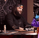 a man with a beard is sitting at a table with a bottle of lotion on it