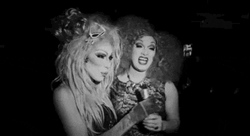 a black and white photo of two drag queens laughing and looking at each other .