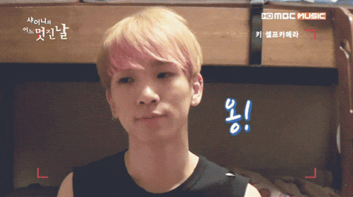 a young man with pink hair is standing in front of a mbc music advertisement